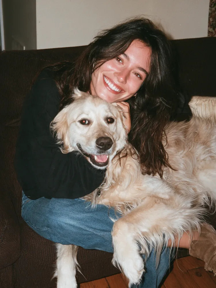 A smiling woman embracing a cream-colored dog at home.